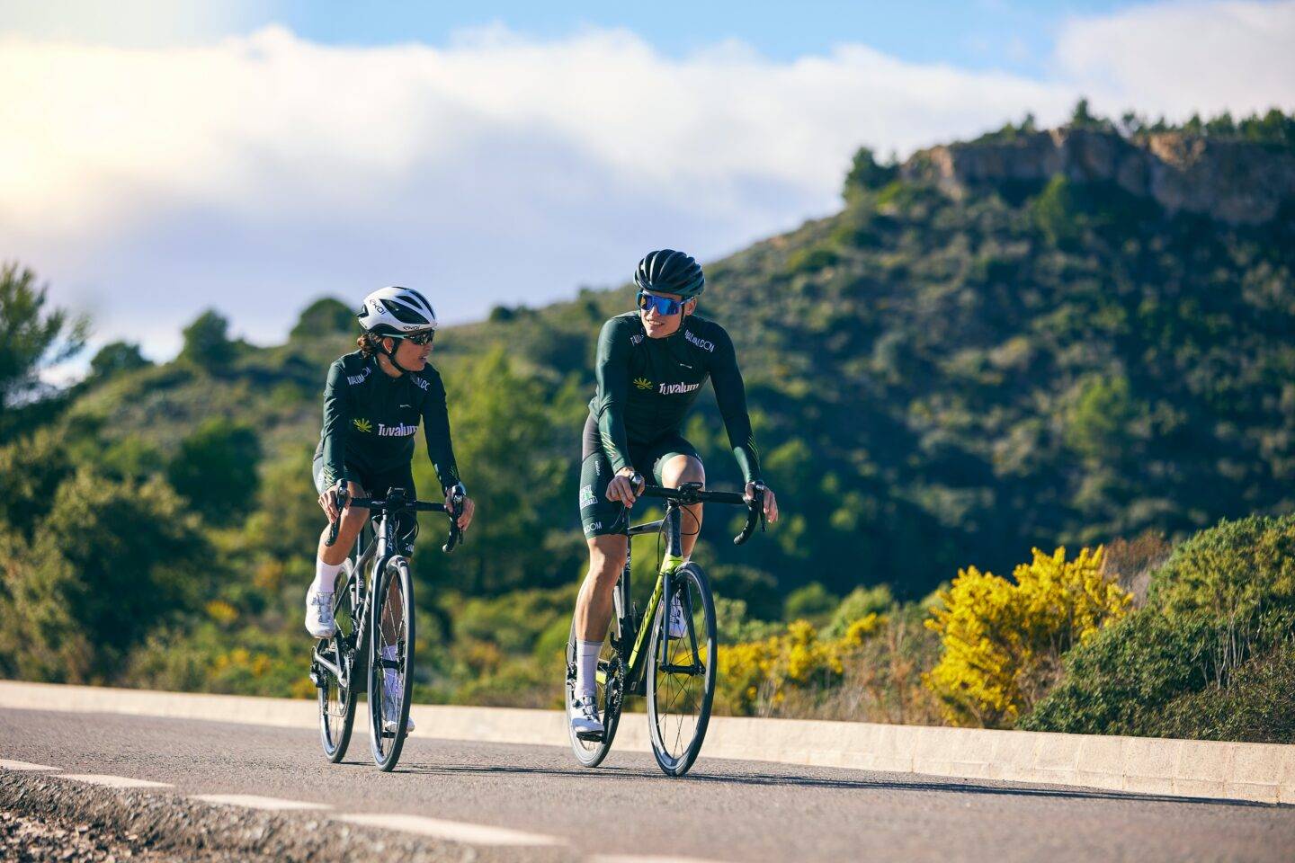 Two cyclists riding down a path with green hills in the background