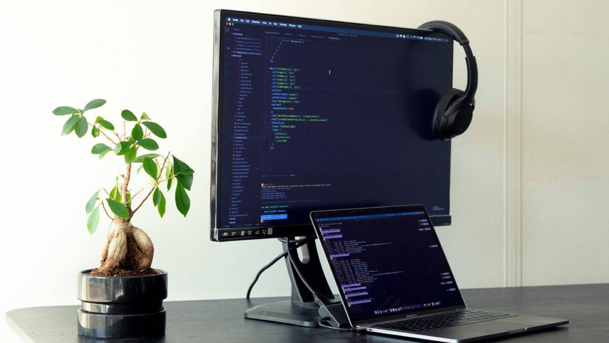A software developer's desk, showing a computer and laptop displaying computer code