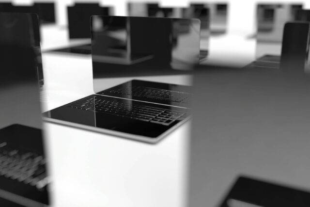 Monochrome close-up of an open laptop on a white desk, surrounded by blurred laptops, creating a sleek, modern technology-focused mood.
