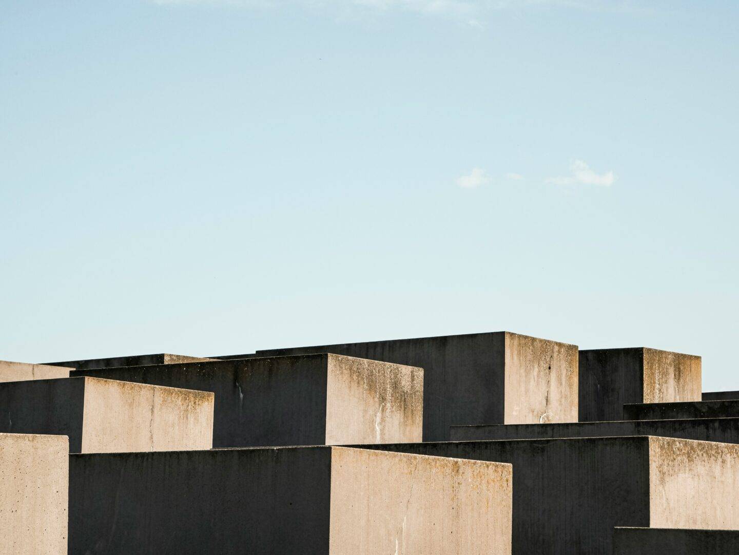 Weathered concrete blocks in black and tan form a stark modern skyline beneath a pale blue sky, creating a calm, austere mood.