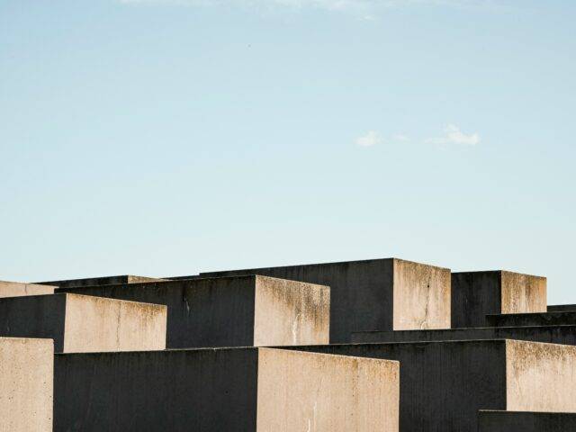 Weathered concrete blocks in black and tan form a stark modern skyline beneath a pale blue sky, creating a calm, austere mood.